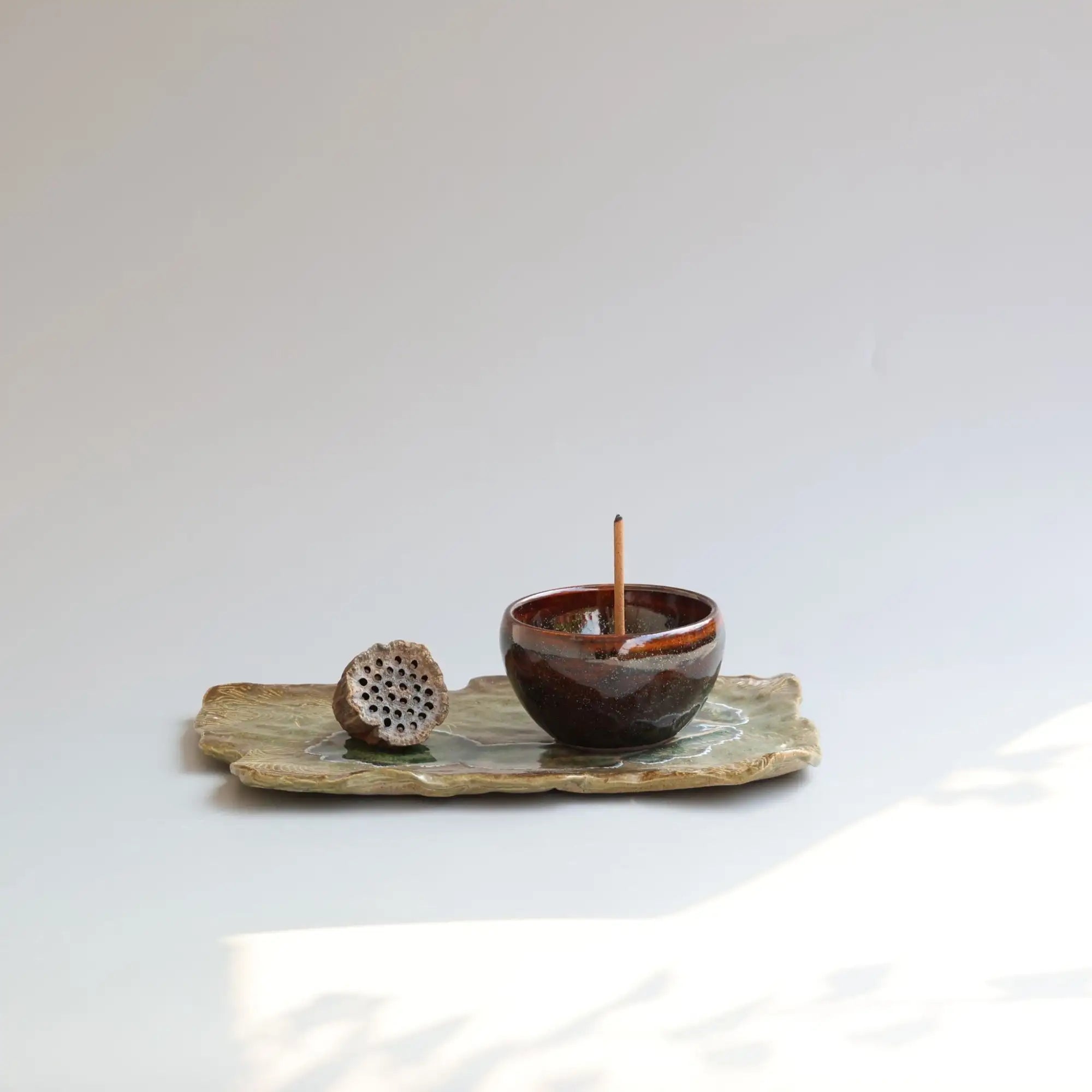 Dark brown ceramic incense burner with a glossy glaze and subtle texture, resting on a matching leaf-shaped tray.