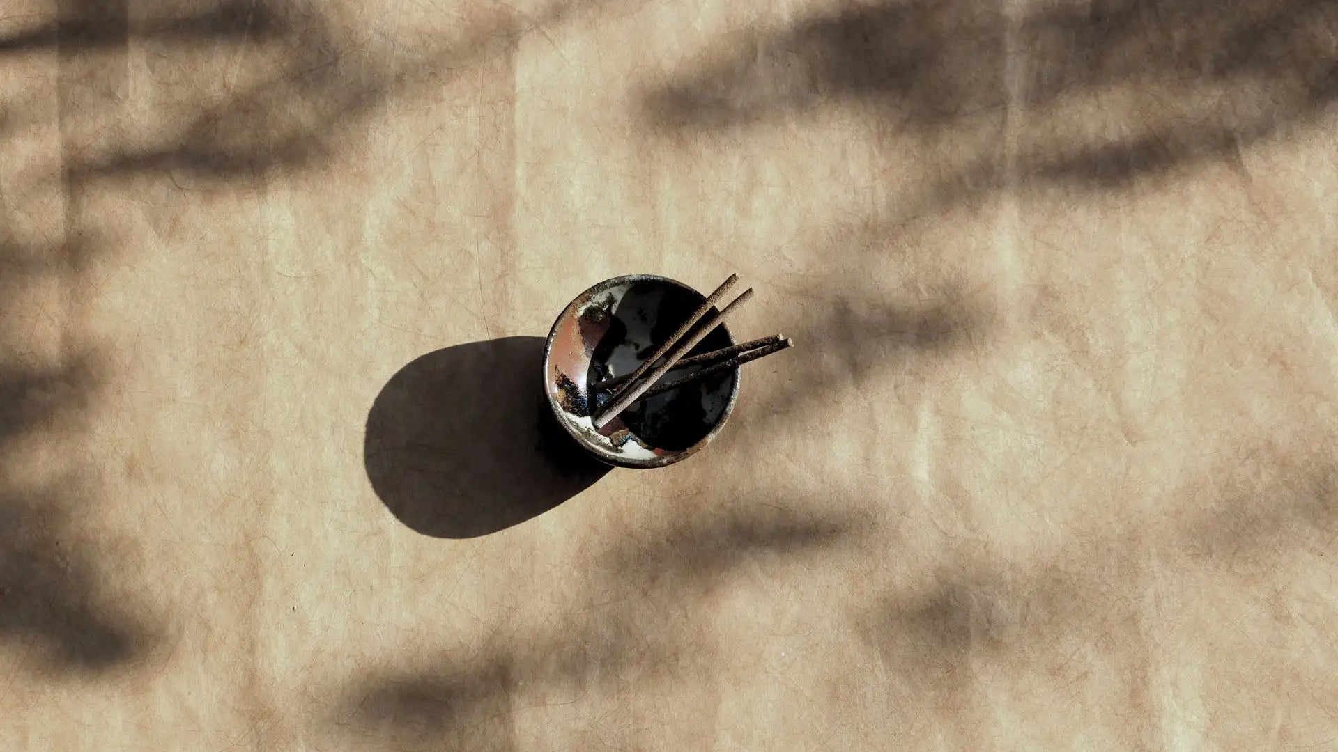 A small, dark ceramic bowl with a glossy finish holds two slender wooden chopsticks.