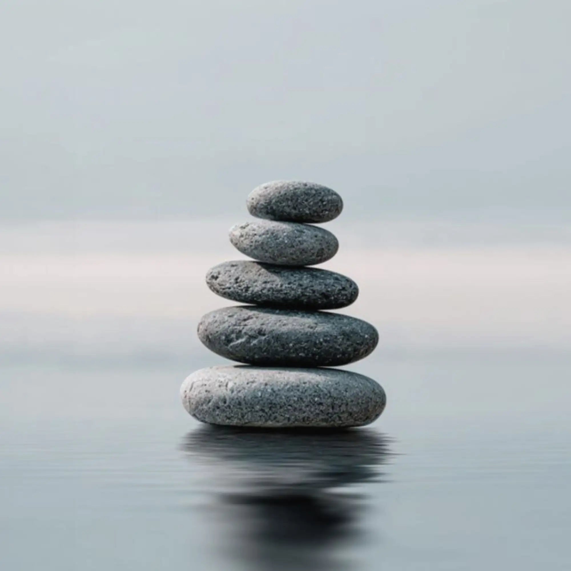 A stack of smooth, rounded gray river stones balanced on a calm water surface.